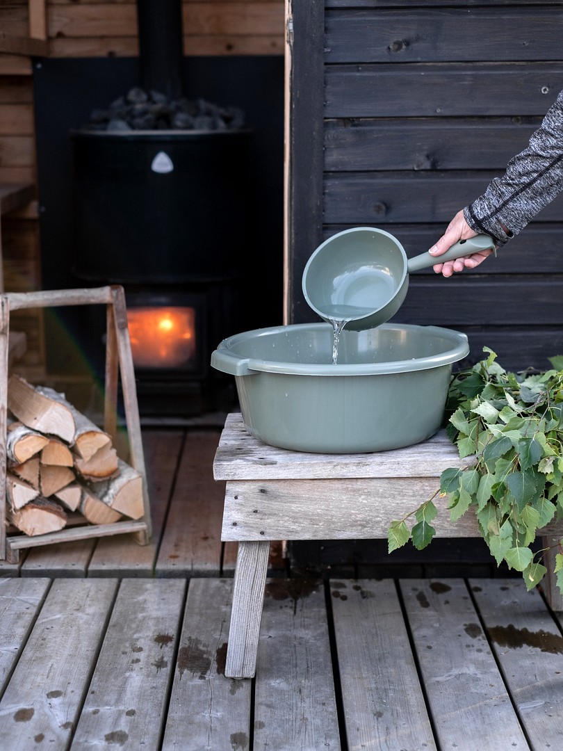 Orthex wash tub on a bench, sauna in the background, hand pouring water with water scoop to the wash tub